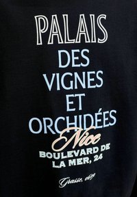 Κείμενο πάνω σε μαύρο ύφασμα: Palais des Vignes et Orchidées Nice Boulevard de la Mer, 24 Grasse, 0630.