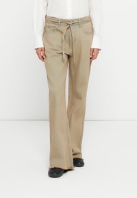 Τα παντελόνια με φαρδιά γραμμή σε καφετί απόχρωση, με ψηλή μέση, διαθέτουν ζωνάκι που δένει, πλαϊνές τσέπες και ακατέργαστο στρίφωμα. Είναι κατασκευασμένα από ανθεκτικό denim ύφασμα.