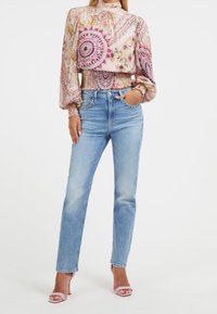 Bluse med blomsterprint, lange ærmer i lys pink med flæser ved håndleddene, parret med lyseblå straight-leg jeans og bløde pink hæle-sandaler.
