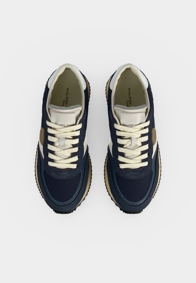 Paire de baskets bleu marine et beige à lacets avec semelles blanches, vues de dessus sur fond blanc uni.