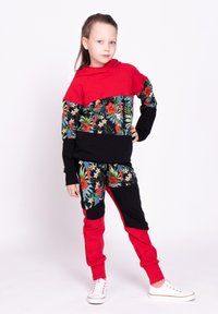 Czerwona i czarna bluza z kapturem w kwiatowy wzór; pasujące spodnie; mieszanka bawełny; wyróżnia się intensywnymi kolorami i graficznymi nadrukami. Białe buty sportowe.