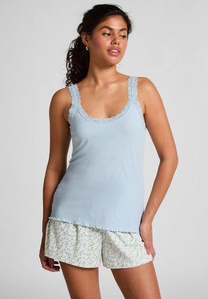 Hellblaues, geripptes Tanktop mit Spitzenrand an den Trägern, kombiniert mit weißen Shorts, die ein blaues Blumenmuster und einen gefransten Saum aufweisen.