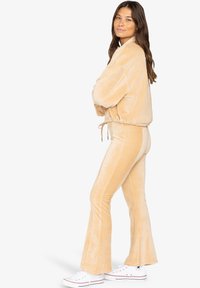 Beige corduroy trainingspak met een cropped, met trekkoord verstelbare jas en flare-pantalons, van een gestructureerde stof, gecombineerd met witte sneakers.