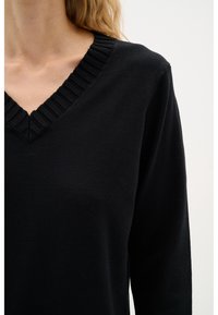 Maglione nero con scollatura a V e dettagli a coste. Maniche lunghe e tessuto morbido e testurizzato.
