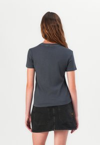 Grå bomullströja med korta ärmar och rundad halsringning, bärs med en svart jeanskjol. Enkel design, jämn textur och fläckfri baksida.