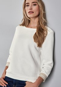 Weißer strukturierter Pullover, Rundhalsausschnitt, Dreiviertelärmel mit kontrastierenden beigen Bünden, lockerer Schnitt, weiche Strickware.