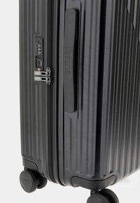 Valigia rigida nera con texture a righe verticali, maniglia resistente, serratura a combinazione, doppia cerniera e ruote che scorrono agevolmente.