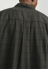 Cămașă cu carouri verzi închise, cu o croială lejeră, având o textură moale, pliere frontală și un design al gulerului.