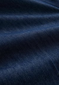 Tessuto in denim blu scuro con trama diagonale visibile e morbide pieghe che creano ombre e luce.