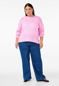 Rosa stickad tröja med rund halsringning och långa ärmar, i kombination med vida blå denimjeans. Slät textur och avslappnad passform.