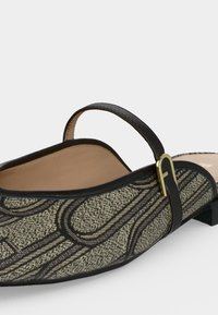 Chaussure plate femme à enfiler en tissu noir et beige à motif chaîne, bordure en cuir noir et petite bride à boucle dorée sur le cou-de-pied.