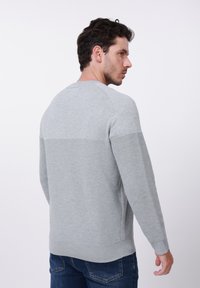 Sweat-shirt gris avec motif côtelé horizontal sur la partie inférieure, encolure arrondie et manches longues. Texture douce et coupe décontractée.