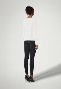 Langärmliges weißes Oberteil und schwarze Leggings, kombiniert mit schwarzen High Heels. Der Stoff ist glatt, enganliegend und elegant und betont die Körperform.