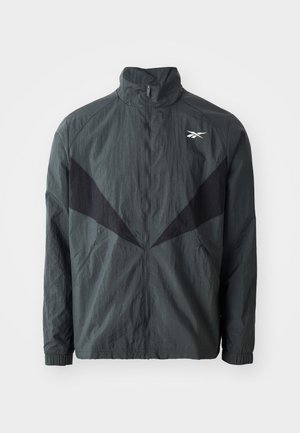 Melna un pelēka jakas ar augstu apkakli, rāvējslēdzējs un elastīgas aproces. Izceļas ar strukturētu audumu un slīpiem melniem ieliktņiem priekšpusē.