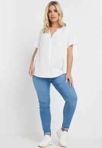Top bianco a maniche corte con scollatura a bottoni e texture orizzontale. Abbinato a jeans skinny blu chiaro e sneaker bianche.
