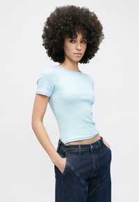 Világoskék bordázott rövid ujjú póló kerek nyakkal, magas derekú sötét farmernadrággal, látható varrásokkal és zsebekkel.