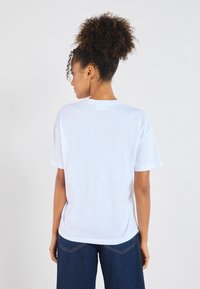 Vit bomull t-shirt med rundad halsringning och korta ärmar, med en avslappnad passform. Bakifrån visas en slät textur och enkel design.