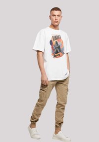 Hvid bomulds t-shirt med et Darth Vader grafisk motiv, parret med beige cargobukser med sidelommer og elastiske manchetter, båret med hvide sneakers.