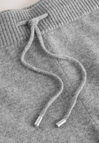 Gray cotton sweatpants featuring a ribbed waistband and flat drawstrings with silver metal tips, showing a soft, textured fabric.