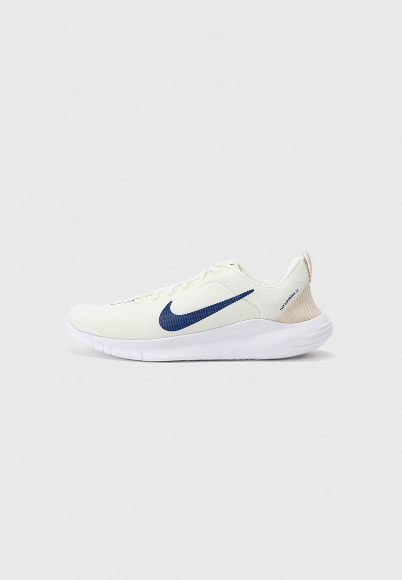 Chaussure de running Nike blanche avec logo swoosh bleu marine et languette beige au talon, présentée sur un fond gris clair uni.