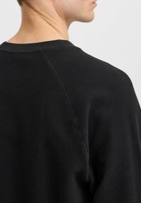 Hanorac negru din material texturat, cu un model în vafe, având guler rotund și mâneci raglan, prezentând detalii de cusătură la umeri.