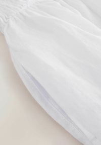 Tissu en lin blanc avec un détail de poignet ou de jambe de pantalon élastiqué froncé, montrant des coutures nettes et une texture légère.