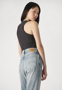 Čierny rebrovaný top bez rukávov v kombinácii so svetlo modrými džínsy s vysokým pásom, ktoré majú štítok vzadu. Hladká textúra a čisté línie.