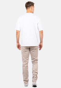 T-shirt blanc à manches courtes, coupe décontractée, associé à un pantalon en velours côtelé beige. Le pantalon présente une texture côtelée discrète et des poches standard.