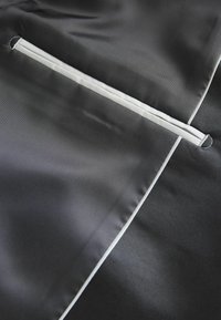 Schwarzer Stoff mit glatter Textur, ausgestattet mit einer weißen Reißverschlusstasche und kontrastierendem weißen Paspel entlang der Kanten.