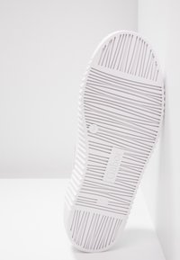 Semelle d'une chaussure blanche avec un motif de sculpture linéaire, nom de la marque Gabor, et détails en relief "Fabriqué en Slovaquie".