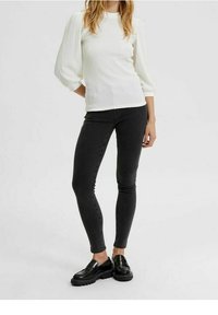 Camisetta bianca a maniche lunghe con texture e maniche a sbuffo, abbinata a jeans skinny neri e mocassini neri chunky. Design semplice e aderente.