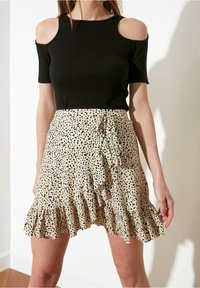 Zwart geribd topje met schouderuitsparingen, gecombineerd met een beige rok met een gerimpelde zoom en een zwart gespikkeld patroon.