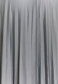 Ljust grått plisserat tyg med vertikala ränder, som visar en mjuk textur. Plisseringarna skapar djup och rörelse i materialet.