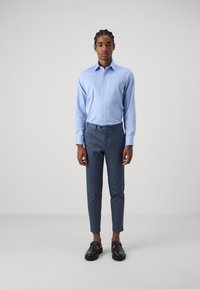 Lichtblauwe overhemd met lange mouwen, gecombineerd met donkerblauwe op maat gemaakte broek en zwarte schoenen, wat een verzorgde casual uitstraling creëert.