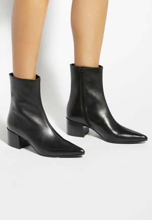 Legs wearing shiny black ankle boots with block heels and side zippers, against a plain white background.