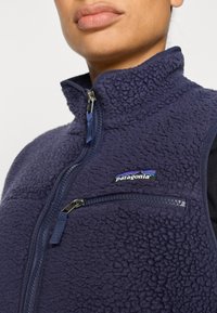 Μπουφάν από φλις σε ναυτικό μπλε με ψηλό γιακά, φερμουάρ μπροστά και τσέπη στο στήθ ος. Διαθέτει υφή και το λογότυπο της Patagonia στο στήθος.