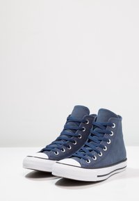 Vysoké tenisky v námořnické modré semišové kůži s bílými gumovými podrážkami, šestihrannými očky a odpovídajícím designem na šněrování; texturovaný povrch a kontrastní špička.