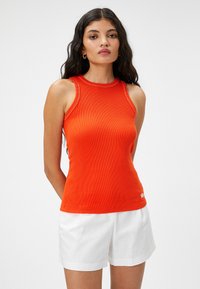 Top arancione a costine con scollatura alta e cuciture bianche a contrasto, abbinato a pantaloni corti bianchi. Tessuto leggero, design attillato.