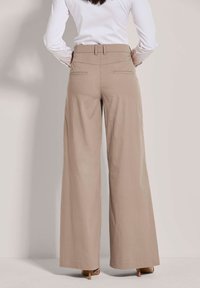 Beige wijde broek met hoge taille, twee achterzakken, een gladde textuur en naaddetails, weergegeven van de achterkant.