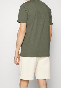 Oliwkowa koszulka z krótkim rękawem i okrągłym dekoltem, zestawiona z jasnobeżowymi szortami. Miękka tkanina, luźny krój, widoczne zawinięte rękawy.