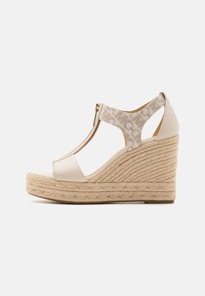 Beige kilehælsandal med flettet jutefodseng, T-rem-design og lynlås på ankelrem med mønstret stofdetalje.
