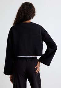 Schwarzes, kurzes Sweatshirt mit langen, weiten Ärmeln. Hat ein einfaches Design und eine weiche Textur, getragen über hoch taillierten schwarzen Hosen.