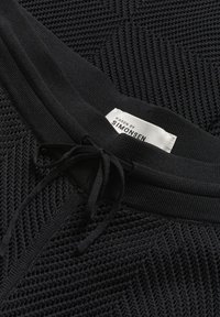 Zwarte gebreide top met een textuurpatroon, voorzien van een trekkoord bij de halslijn en een label met de tekst "KAREN BY SIMONSEN."