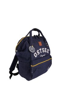 Sac à dos en denim bleu avec une fermeture éclair dorée, logo "OSTSEE Original", poche avant, poignées supérieures et bretelles réglables.