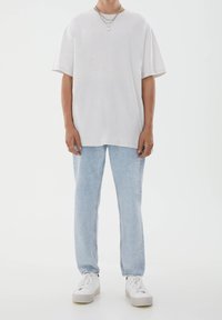 Nadměrné bílé tričko z bavlny s krátkými rukávy, doplněné světle modrými džíny s rovnými nohavicemi a bílými teniskami, s minimalistickým designem.