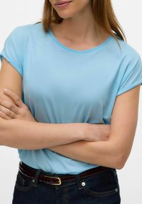 T-shirt azzurro chiaro a maniche corte con scollo rotondo, realizzato in tessuto morbido; abbinato a jeans in denim scuro e una cintura marrone.