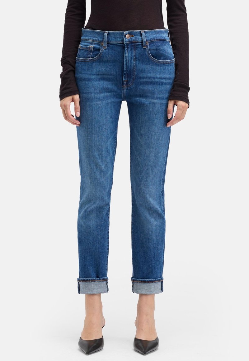 Jean en denim bleu à taille haute, jambes droites et revers retournés. Présente un léger délavage et deux poches avant.