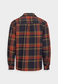 Back view of a plaid flannel shirt in dark blue, red, and olive green. Features buttoned cuffs and a classic collar. Soft texture.