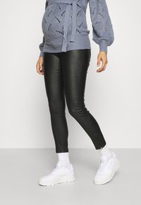 Suéter de punto azul claro con cinturilla anudada, combinado con leggings de cuero sintético negros y zapatillas blancas. Los leggings tienen detalles con cremallera en los tobillos.