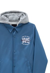 Blå vandtæt jakke med grå hætte. Har en knaplukning foran og et broderet logo, "VANS," med en retro skrifttype og året "Siden Tresseks."